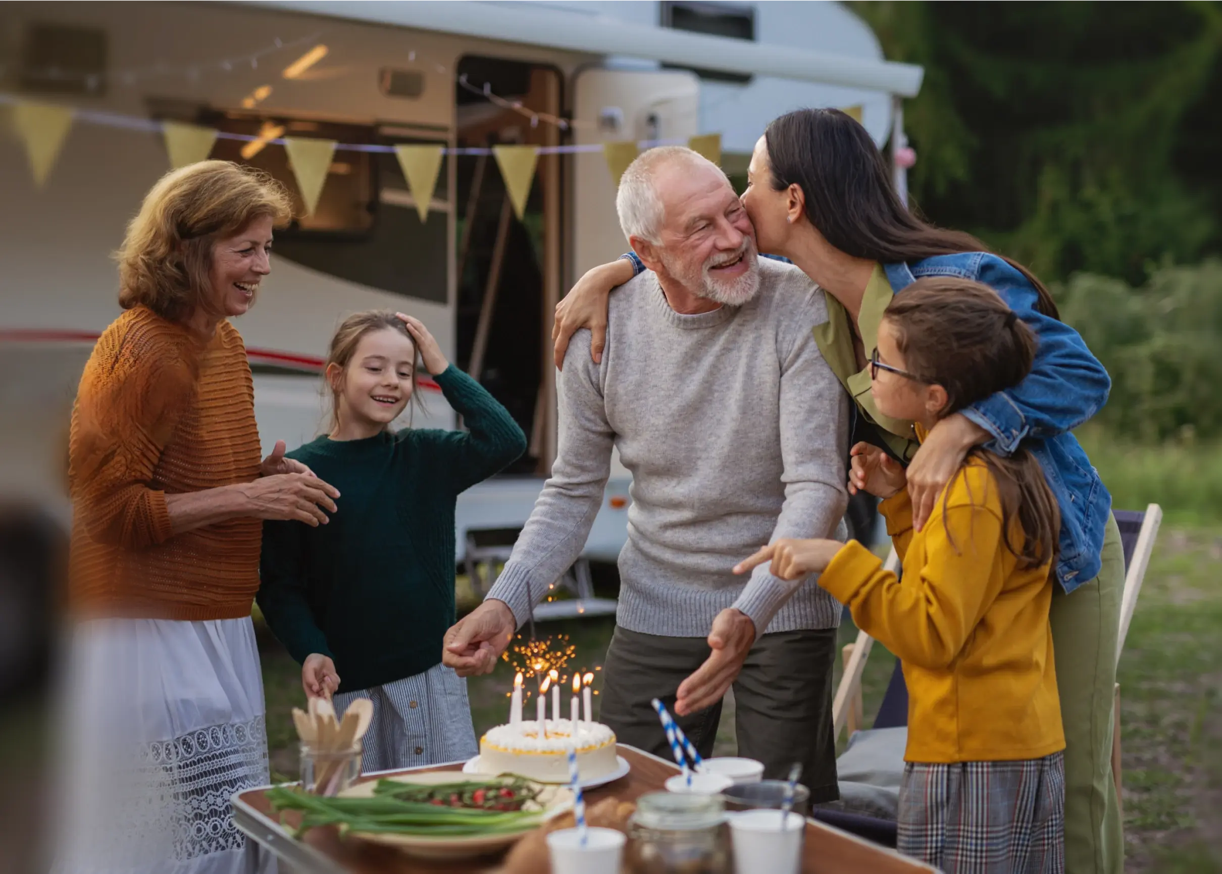 Senior man celebrating birthday outdoors at campsite, multi-generation family caravan holiday trip.